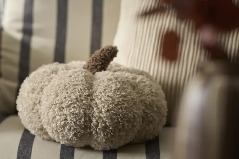 Beige kudde i form av en pumpa ligger på en randig soffa.