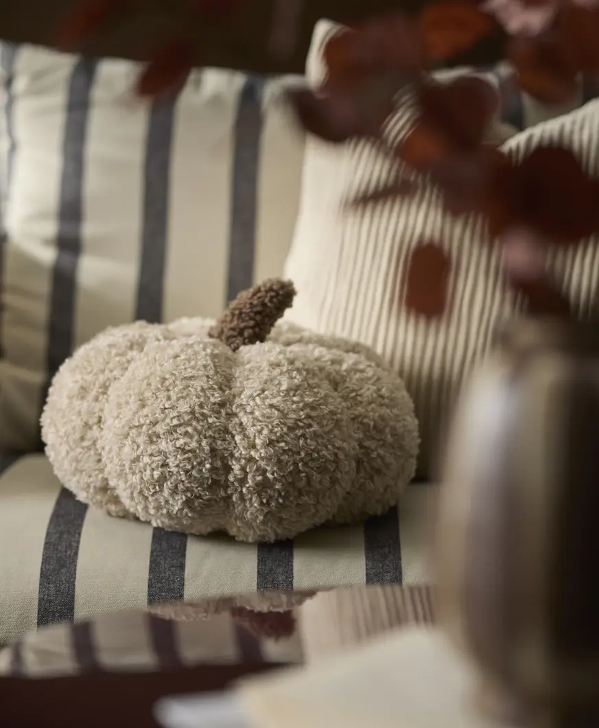 Beige kudde i form av en pumpa ligger på en randig soffa.