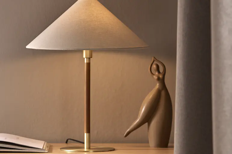 En bordslampa med vit skärm står på en byrå bredvid annan dekoration